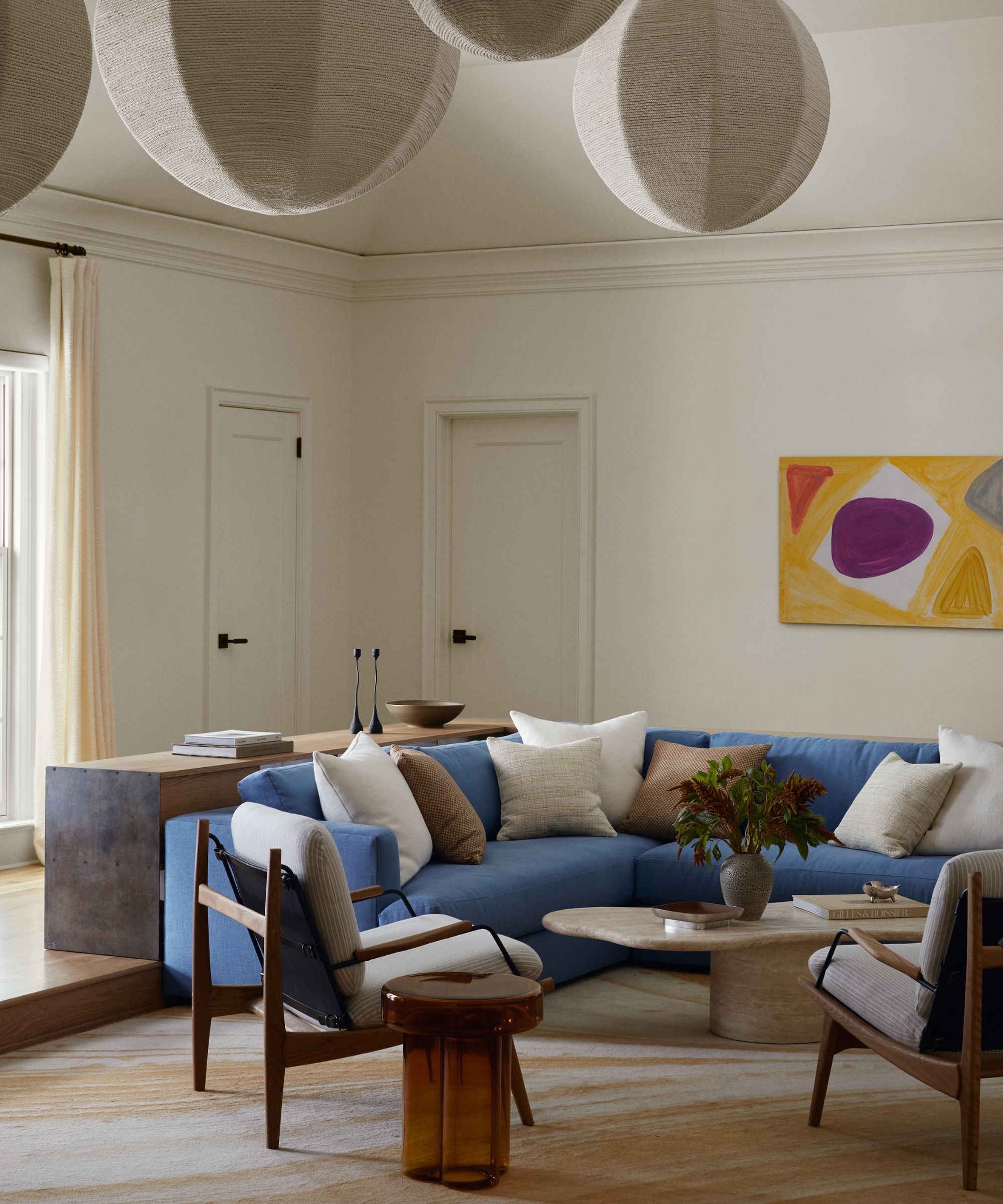White living room with a large blue corner couch, stone coffee table and two beige and wooden armchairs