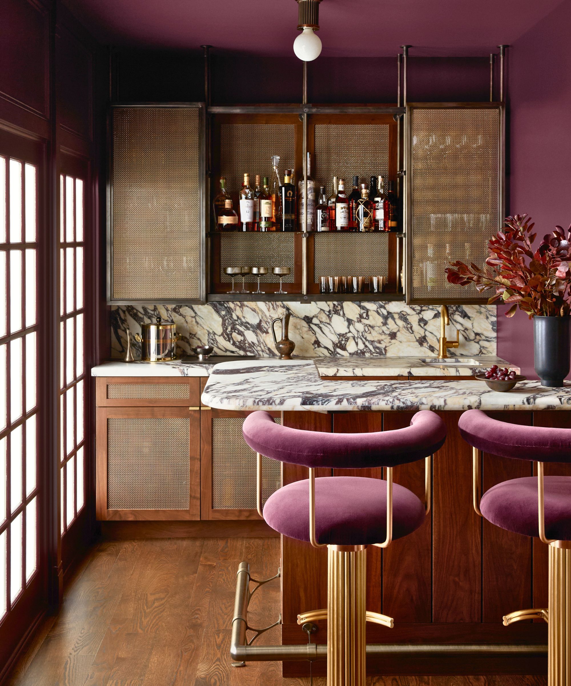 Home bar with dark pink walls, wooden cabinets and marble switches