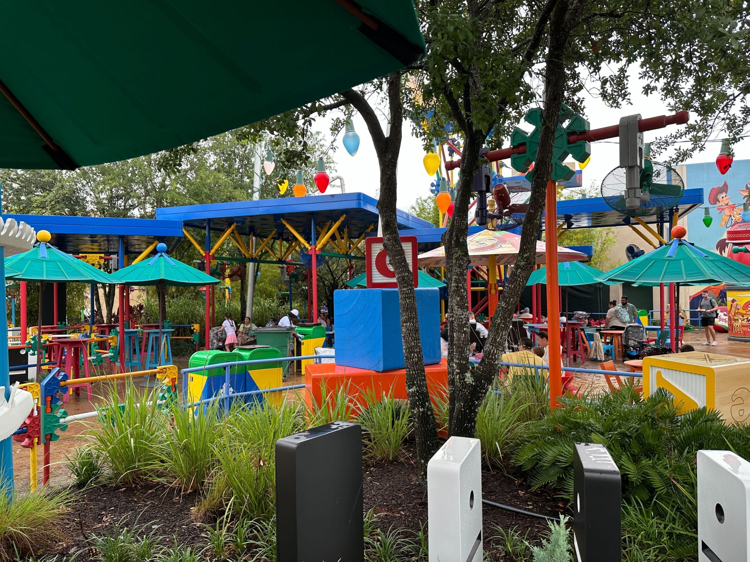 Colorful outdoor seating area with green umbrellas, tables, plants and playful decorations that resemble toys.