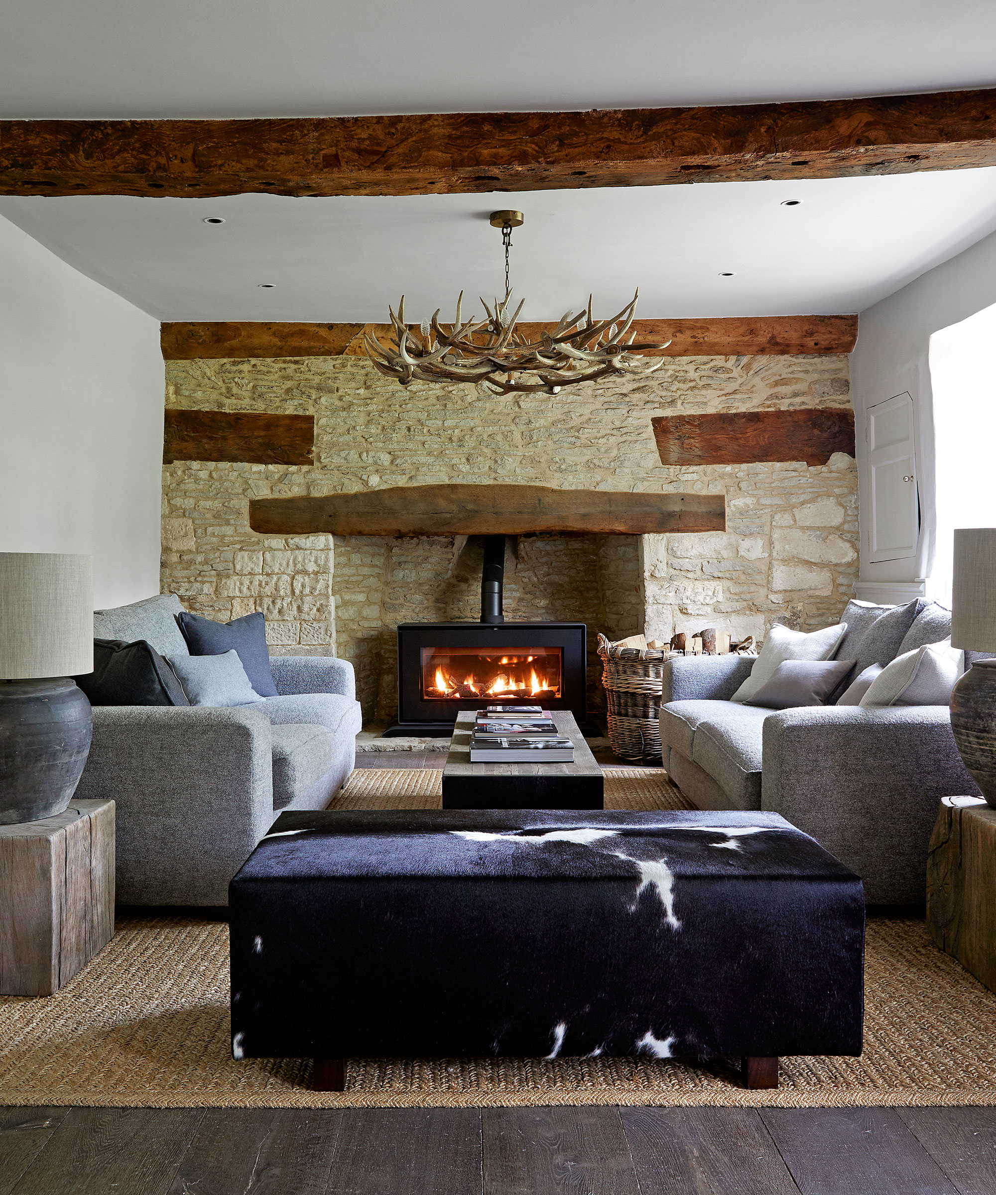Living room with fireplace and exposed stone wall, gray sofa, antlered chandelier and cow delusion shocker