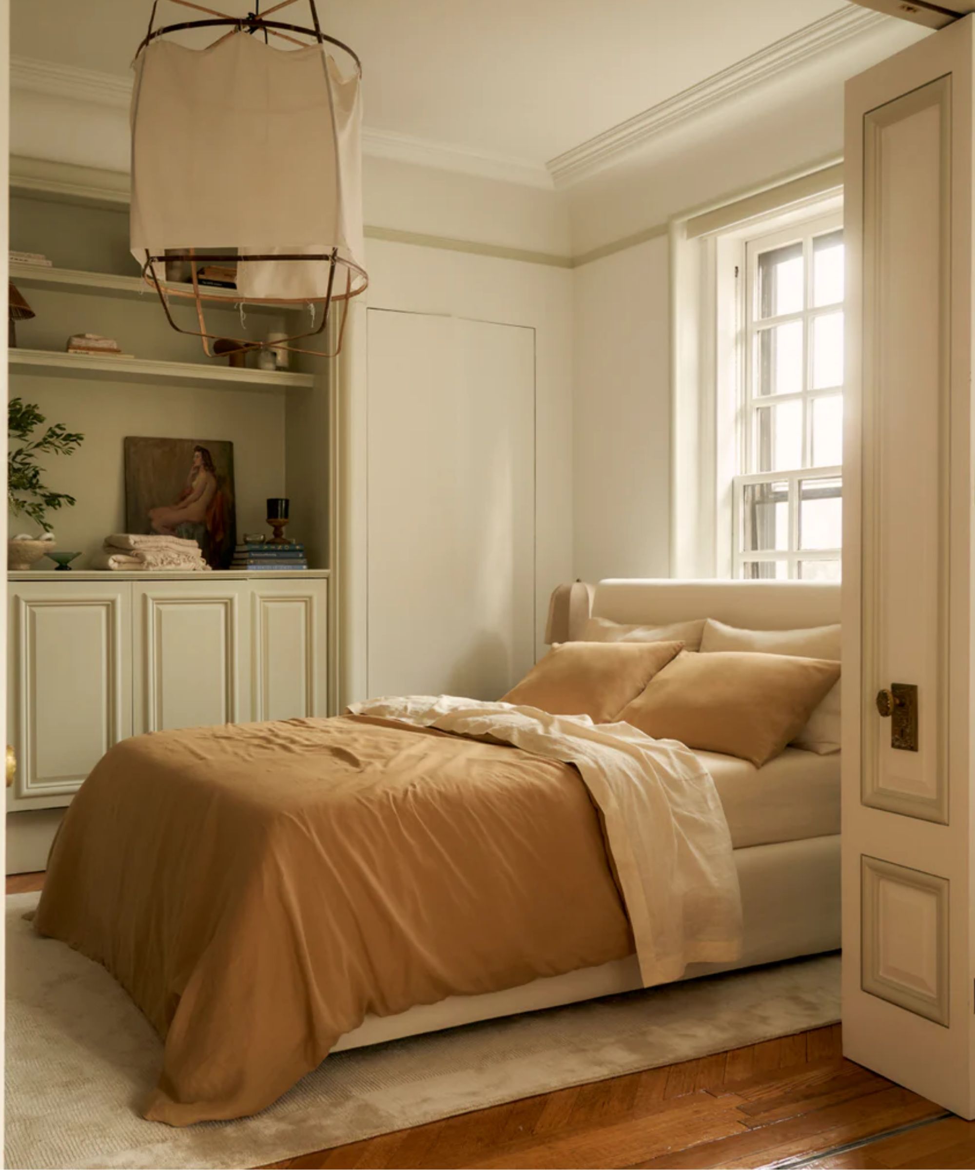 Traditional bedroom room with large decorated doors that lead to the room, a wooden floor, a carpet and a neutral bed with caramel bed linen