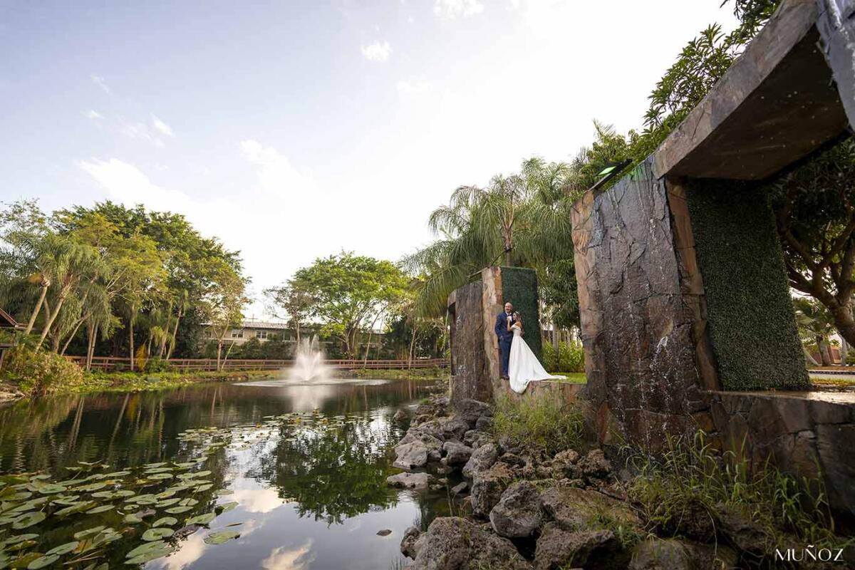 A bride and a groom pose lakeside in the Living Skulpture Sanctuary.