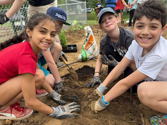 The students smile with their hands in the dirt.