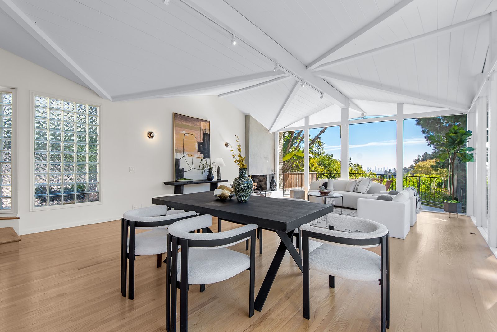 Black dining table with white chairs window line walls living area in the background with white sofa glass block wall ...