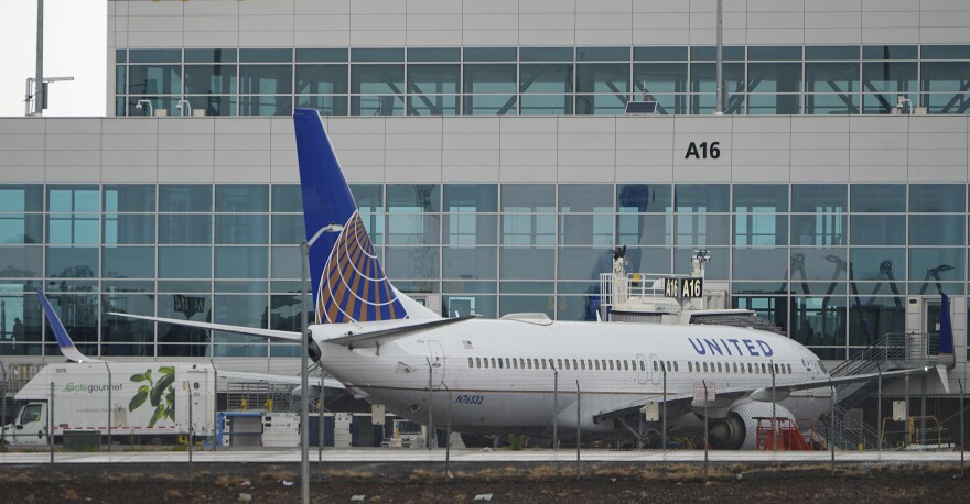 A white level with a blue cock that says "UNITED" On the side sits behind a barbed wire fence in front of a building with large glass windows.