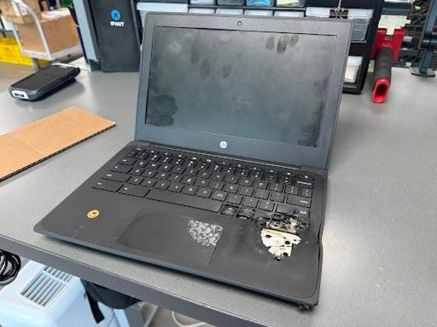 A black laptop on a desk has a large burned point near the keyboard, which is obviously damaged.