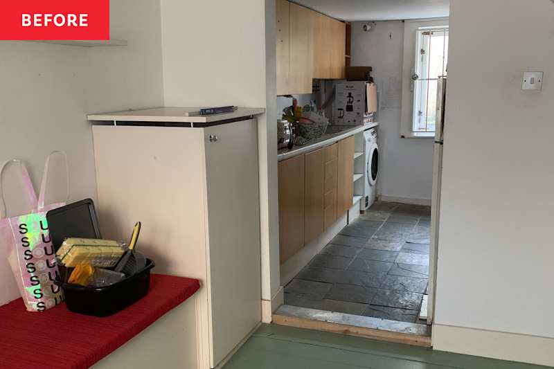 A small kitchen area with wooden cabinets, a washing machine and a worktop overcrowded with utensils and a colorful bag.