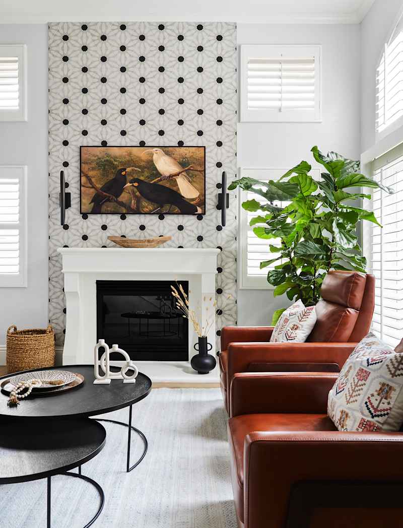 Cozy living room with two brown leather chairs, a black coffee table and a large plant next to a decorative fireplace.