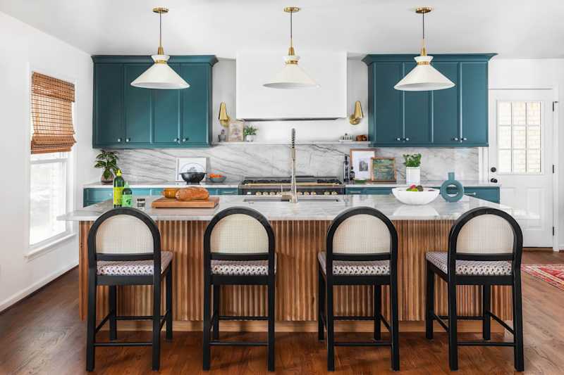 Modern kitchen with blue -green cupboards, marble slabs and wooden stools with a loaf made of bread and decorative bowl.