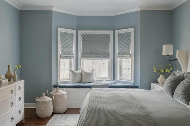 Cozy bedroom with blue walls, a window seat, patterned colors, a white chest of drawers and woven baskets.