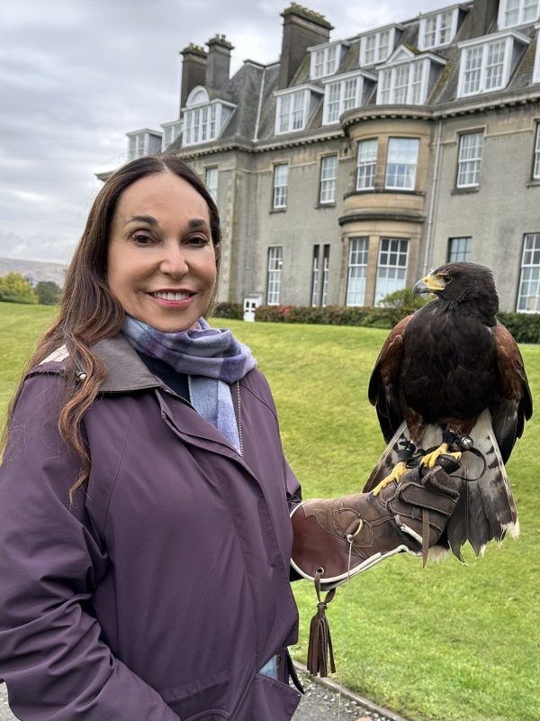 Gail Morris in a purple jacket in a green field with a bird on her arm.