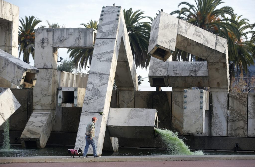 A man and his dog go to the monumental Vaillancourt fountain in San Francisco, a square public sculpture made of concrete, with running water