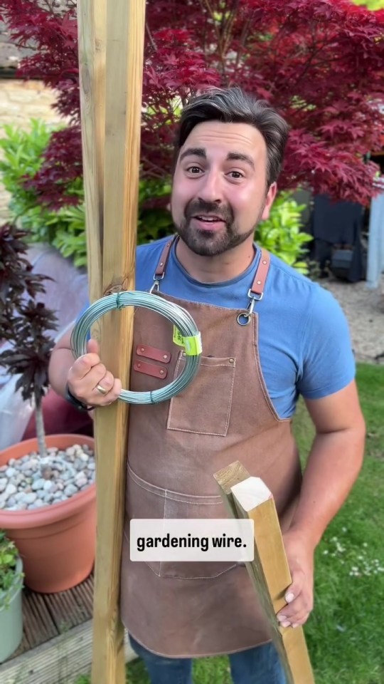 Man holds garden wire and wooden posts.
