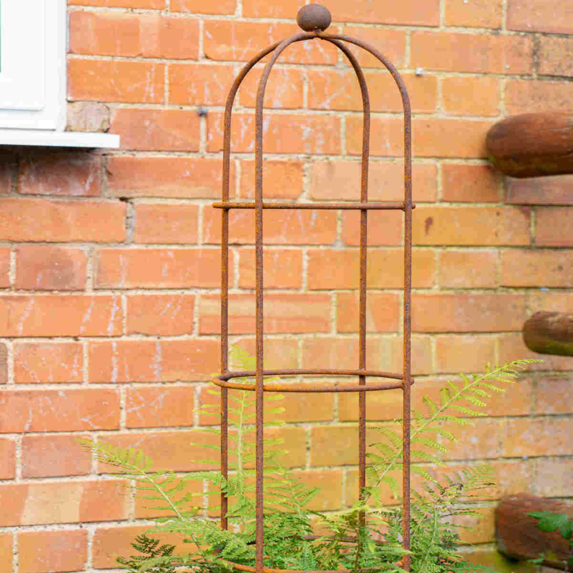 Hayloft Round Obelisk supports a fern near a wall in a garden