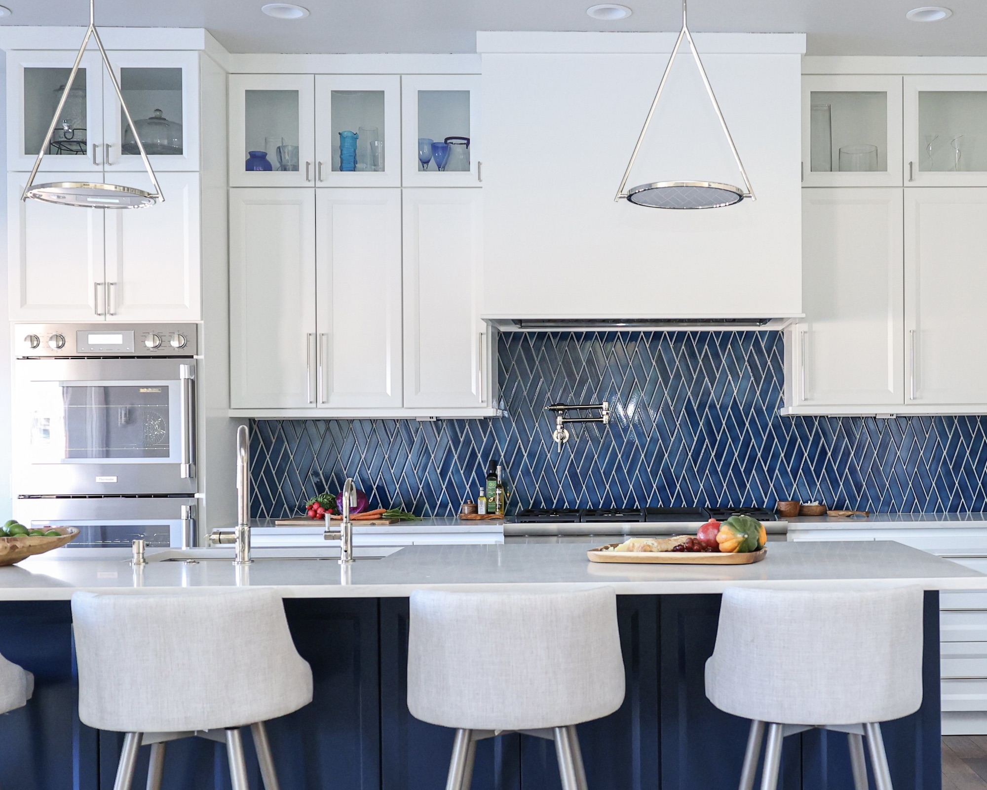 Kitchen with white cupboards and blue island with padded barhoses, white meters and blue geometric back splash