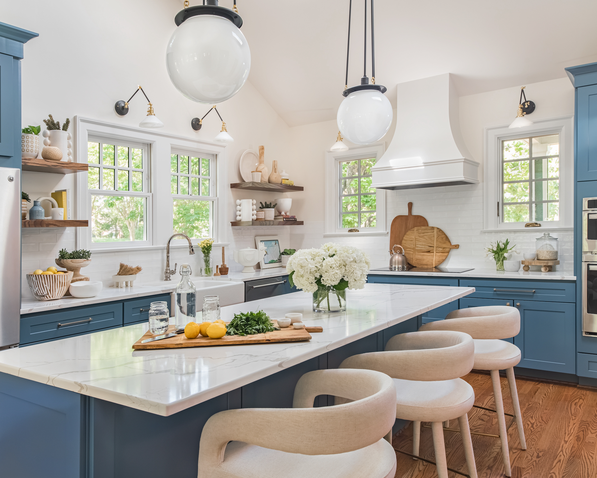 Kitchen with blue cupboards, light worktops, island with trailer lights, padded stools and wooden floor