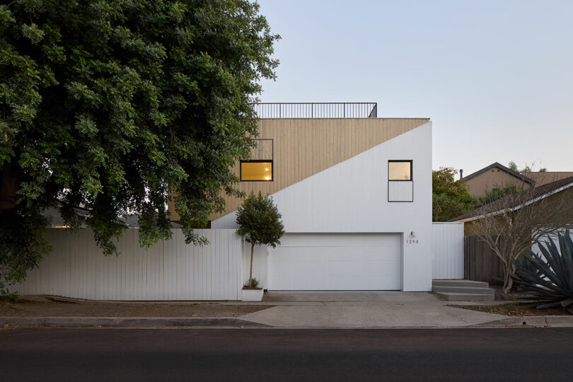 Modern two -story house with a geometric facade, combined wood and white panels, a central garage, rectangular windows and minimal landscape design.