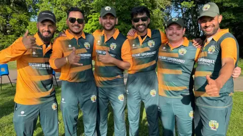 Syed Abbas combines six men and make hand gestures towards the camera. They wear a sports uniform - which is orange and green - and represents the cricket team for which they play.