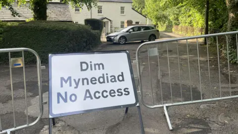 An access sign that connects barriers in front of a house with a silver car outside.