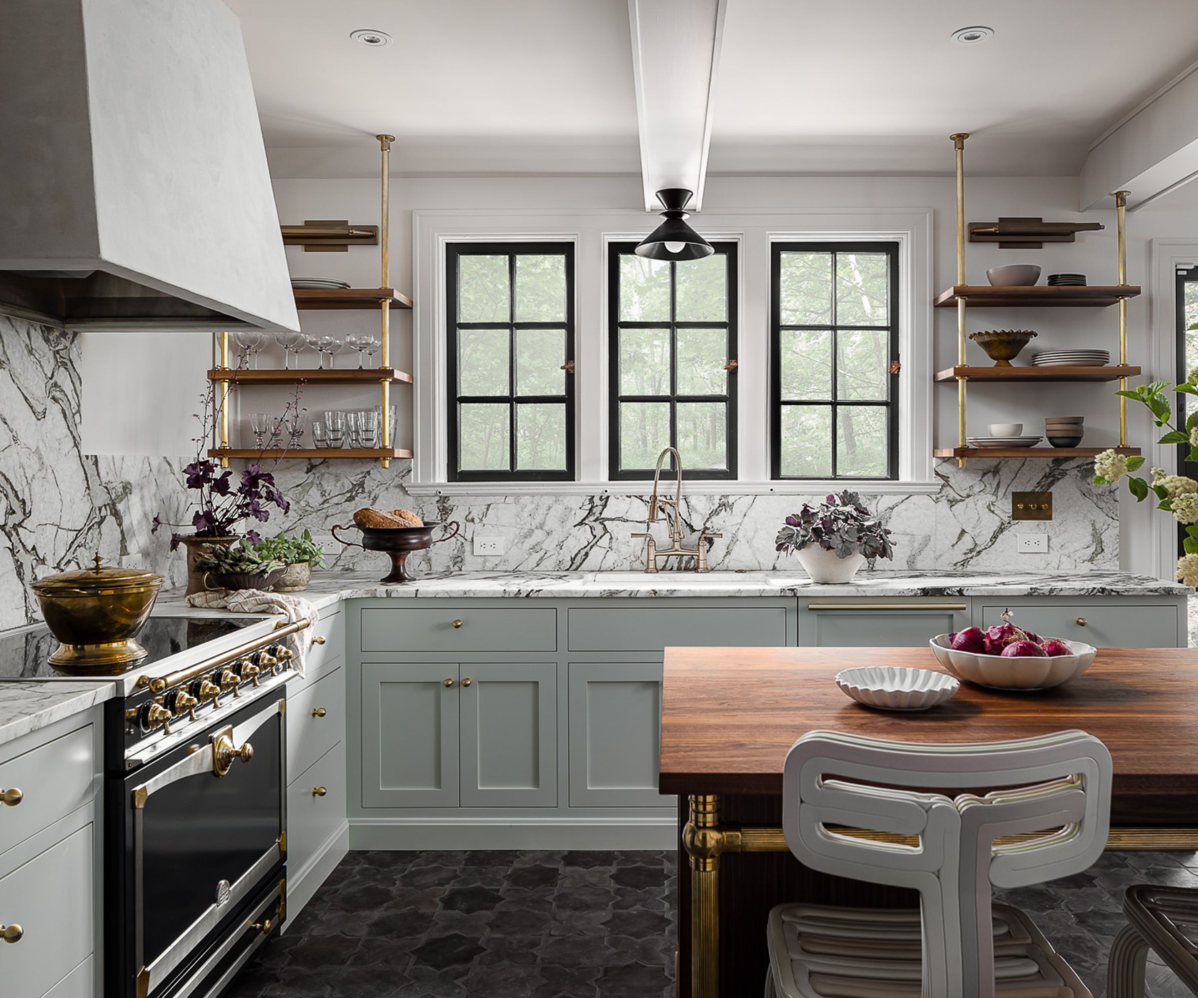 An L-shaped cuisine with a wooden kitchen island, light gray-green cupboards, marble worktops and back splash as well as a black and golden stove