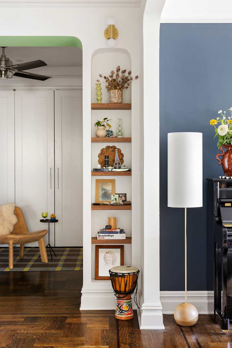 Narrow bookcase with decorative objects, a white lamp and a brown chair in a cozy living room.
