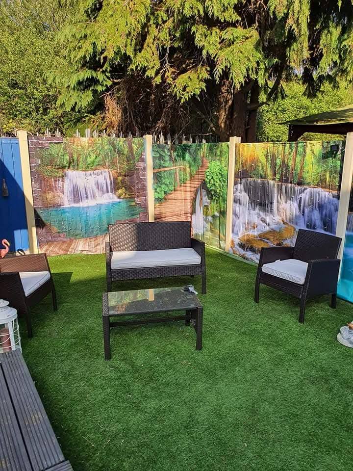 Garden furniture on artificial grass in front of a fence with a waterfall scene plates.
