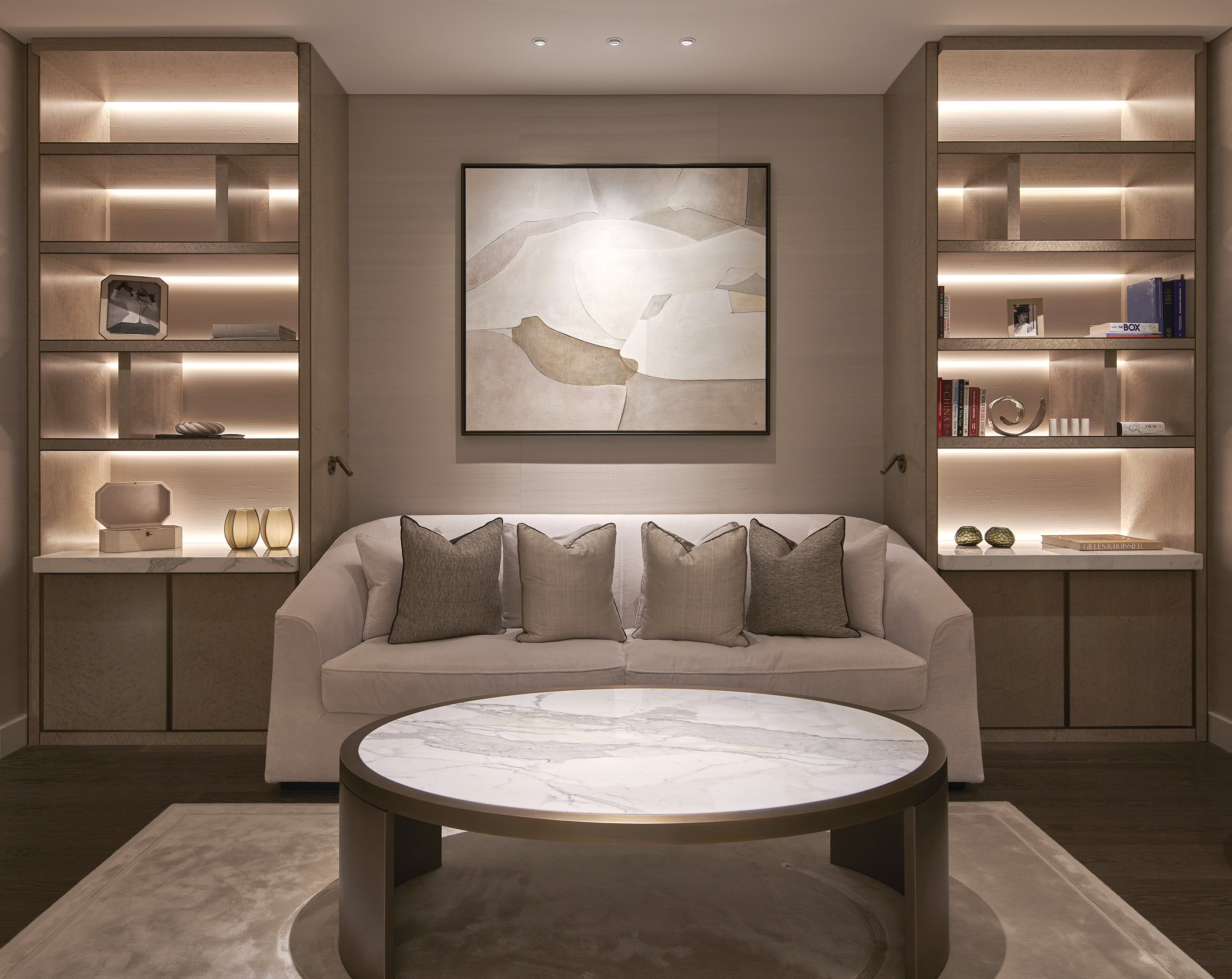 Neutral colored living room with carpet, coffee table, sofa, central wall art and LED backgrounds with decorative objects.