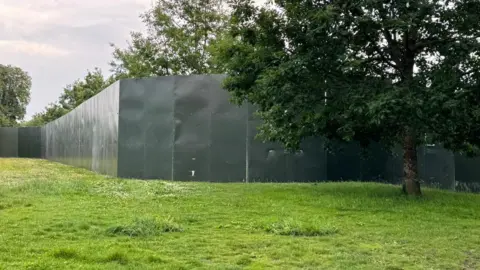 BBC to see a metal wall on a field with a tree in front of it