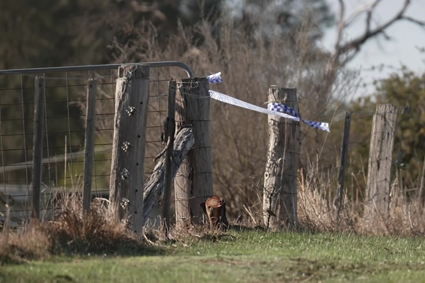 Blue and white checked police band between two posts with an open farm gate.