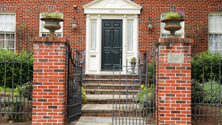 A wrought -iron fence and a gate is in front of a pretty colonial brick house house