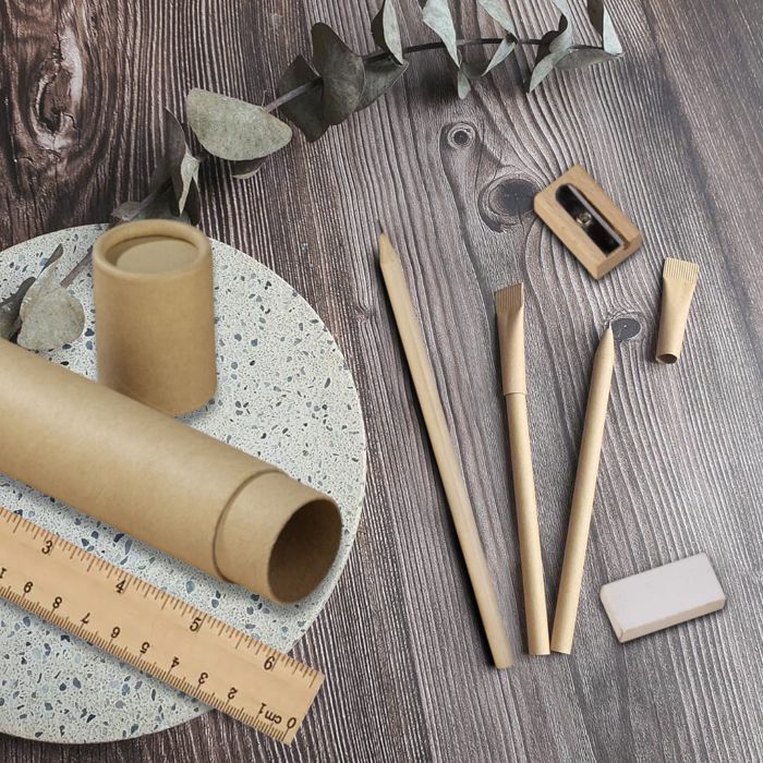 A number of environmentally friendly supplies, perfect for school with wood pencils, a pointer, a etching rubber, a ruler, paprohre and dried eucalyptus leaves arranged on a wooden surface.