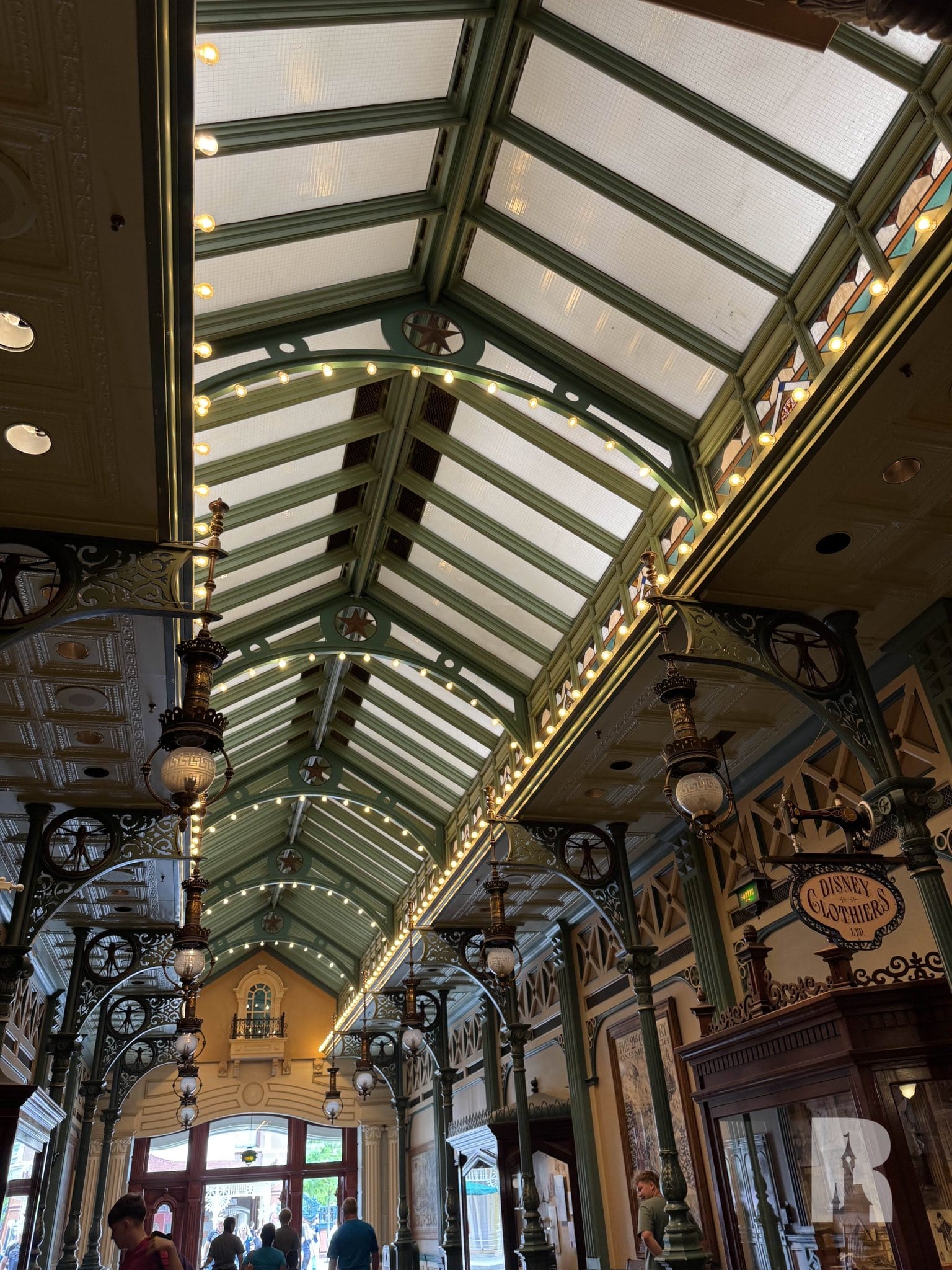 Covered arcade with decorated green metal beams, skylights, hanging lamps and glass ceiling, which lead to an input outdoors.