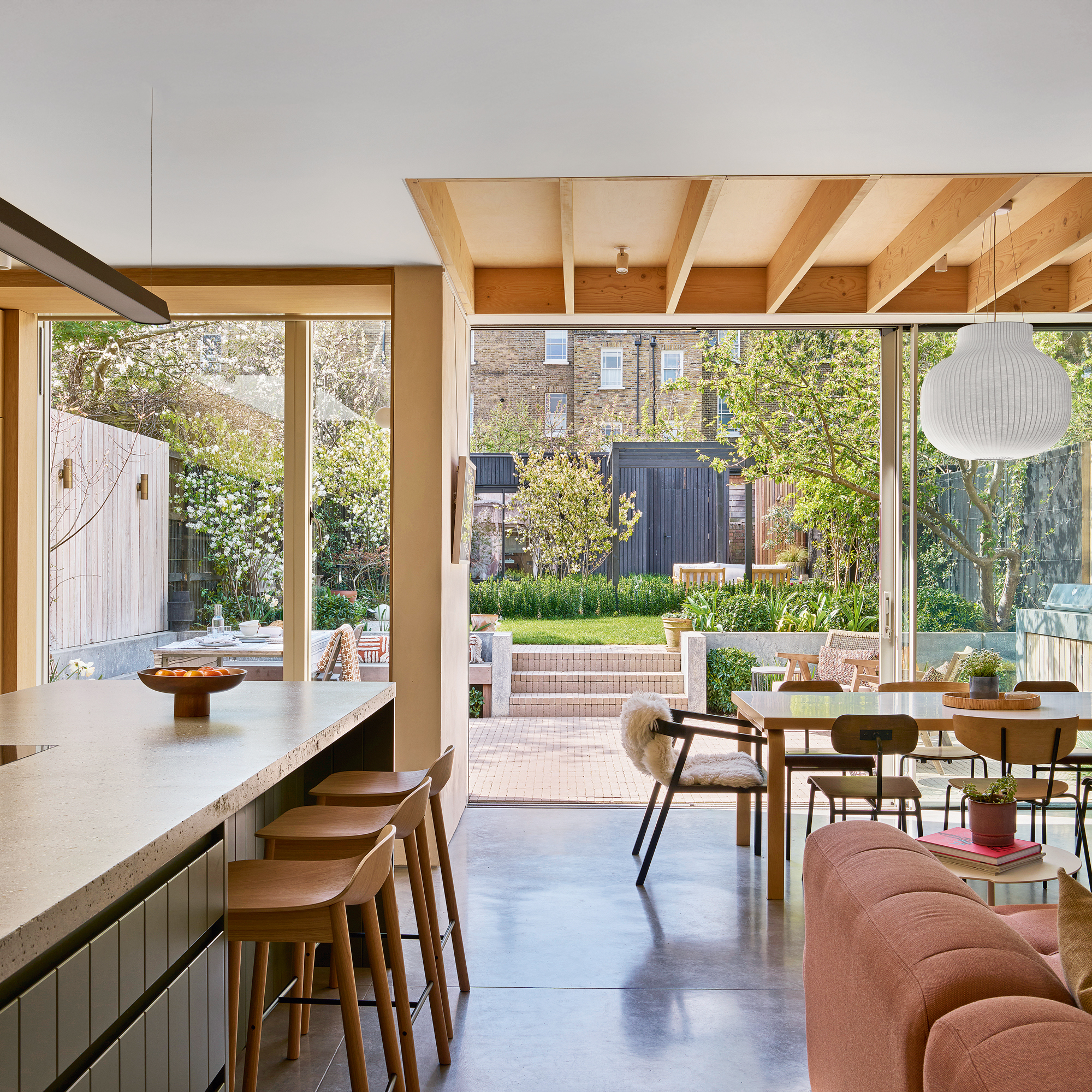 An open kitchen, a dining and living area with supple roof panels, a dark pink sofa and a large kitchen island