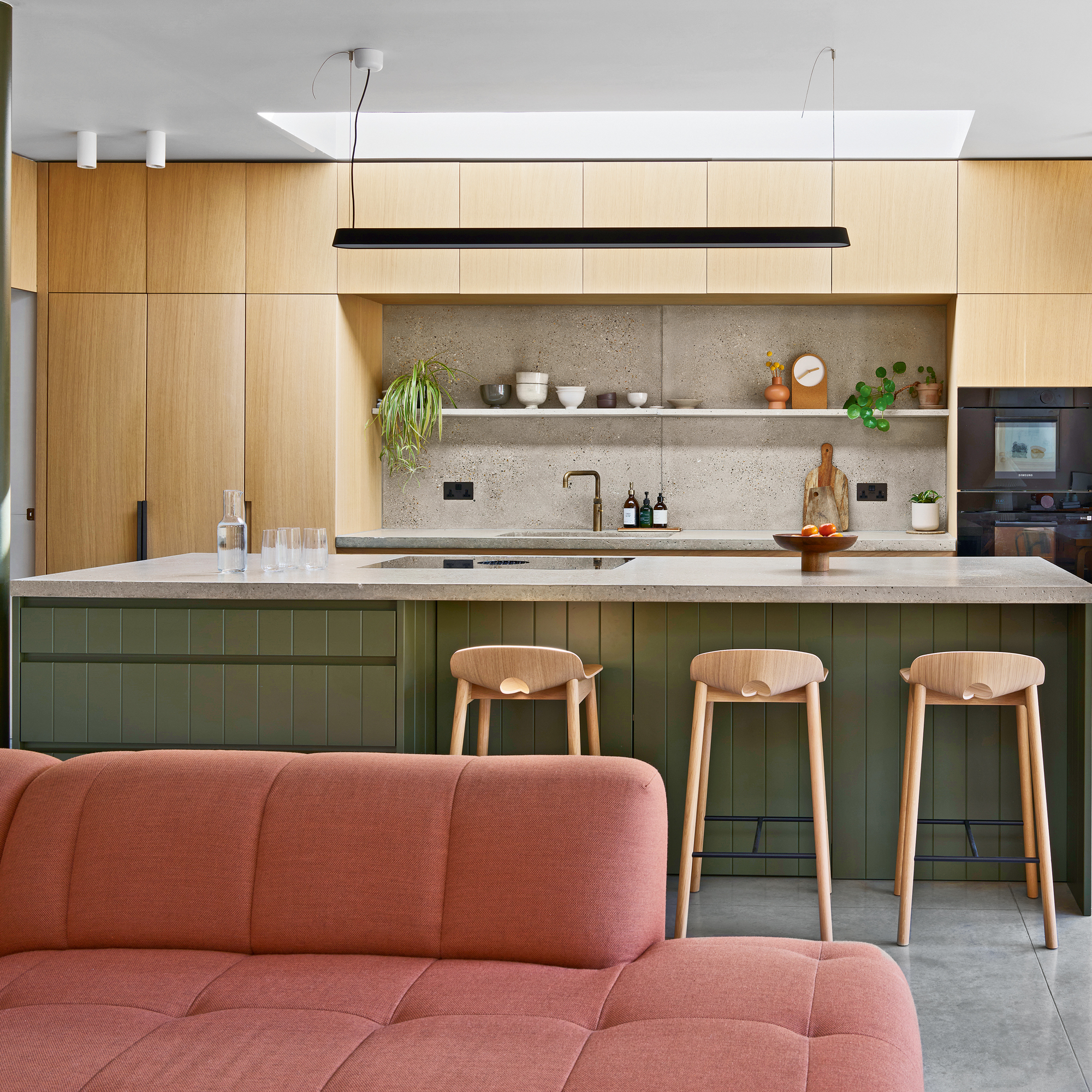 An open kitchen and a living area with a dark pink sofa and a large kitchen island with three bar stools