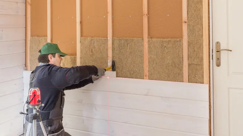 Workers install natural fiber insulation and wooden plate in a half -built wall frame