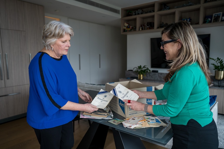 Two women in an apartment look at documents in a box at the dining table.