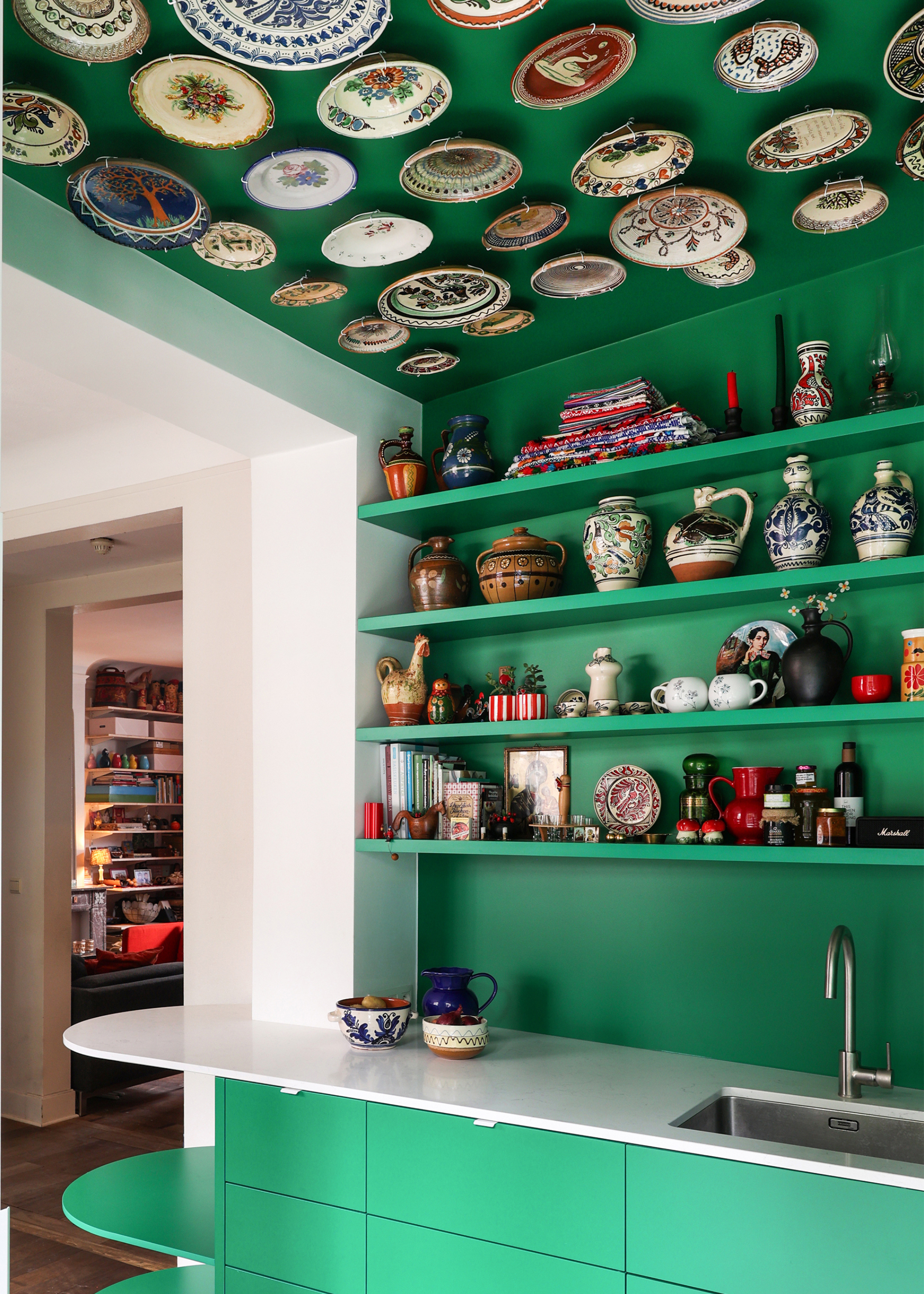 A close -up of a small green kitchen with shelves with a collection of pottery and art