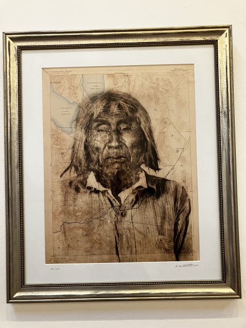 Framed works of art that represent an older man with long hair printed on a sepia topographic map that is displayed on a white wall.