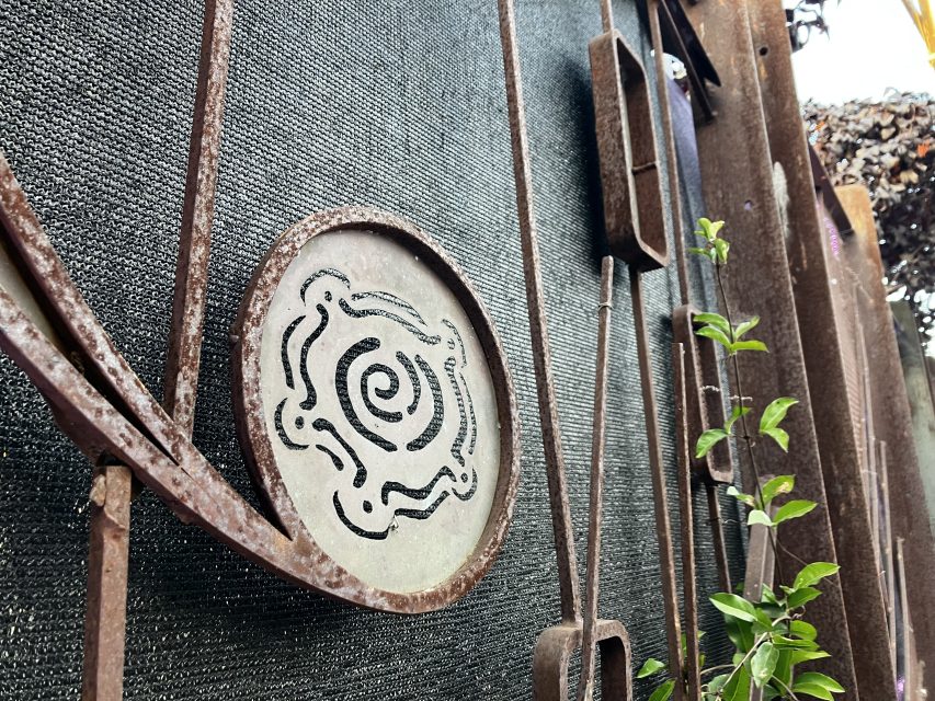 Close up of a rusty metal goal with a circular decorative pattern with green plant leaves nearby.