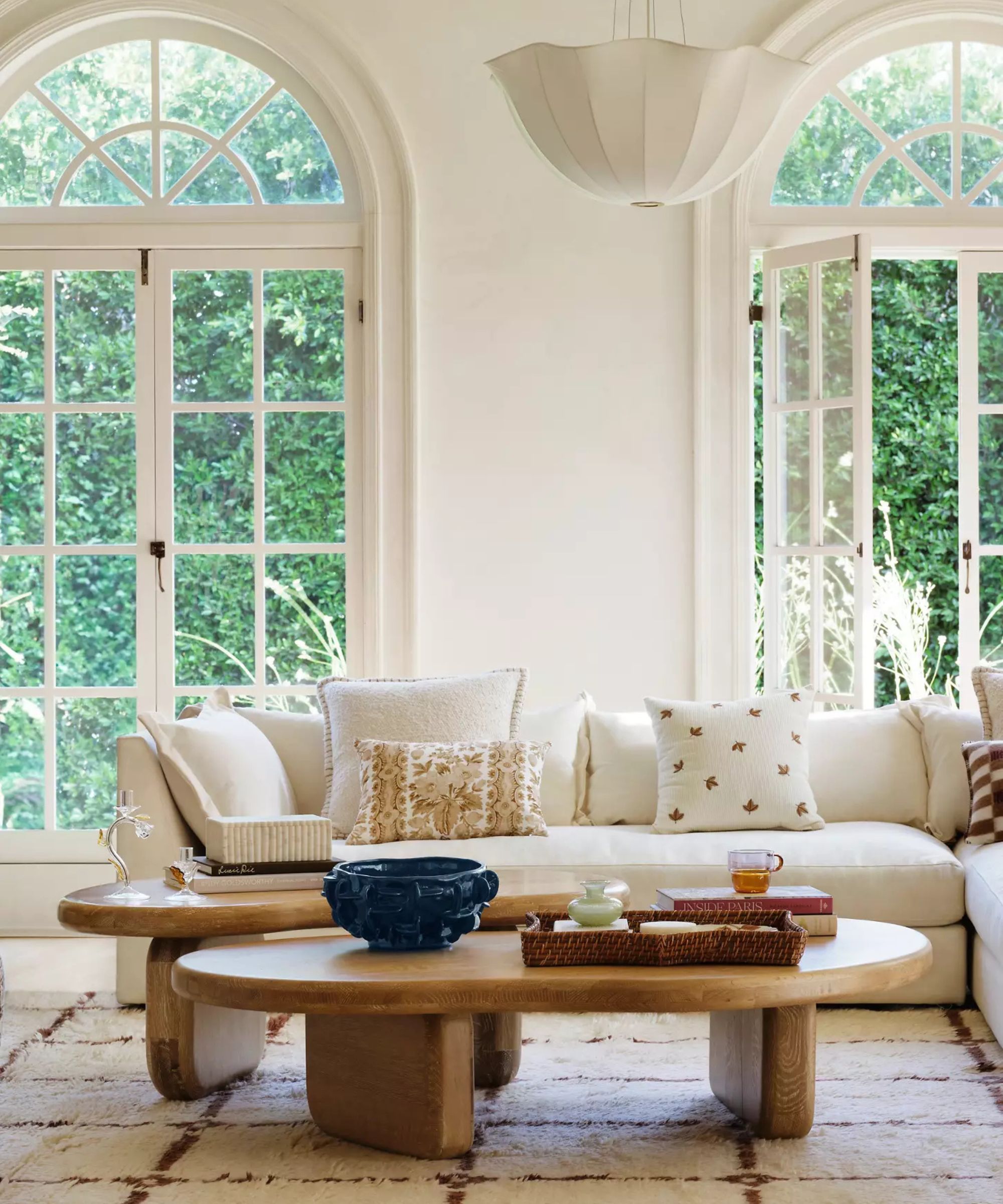 Cern living room with large arched windows, a cream -colored corner sofa with throwing cushions and two wooden coffee tables