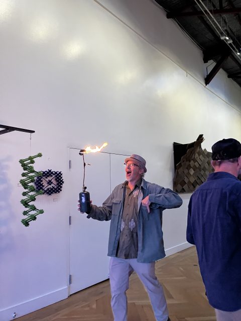 At the end, a man holds a device with a flame and stands in an inner galeric space with tricks on the white wall.