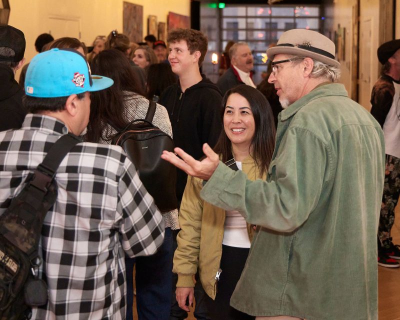 A group of people comprises and talks to an art gallery, with works of art on the walls in the background.
