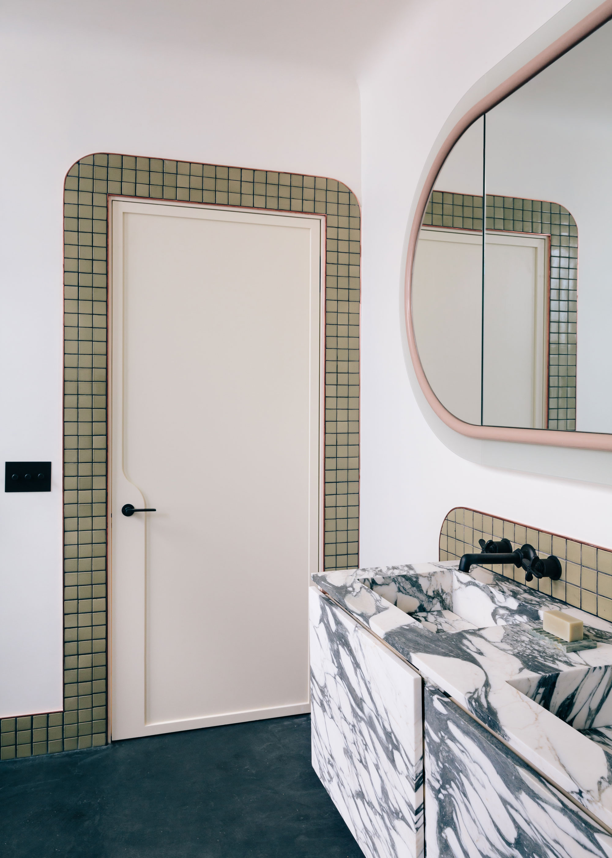 A bathroom with a green tile cladding around the door in a bathroom where two marbled sinks also had