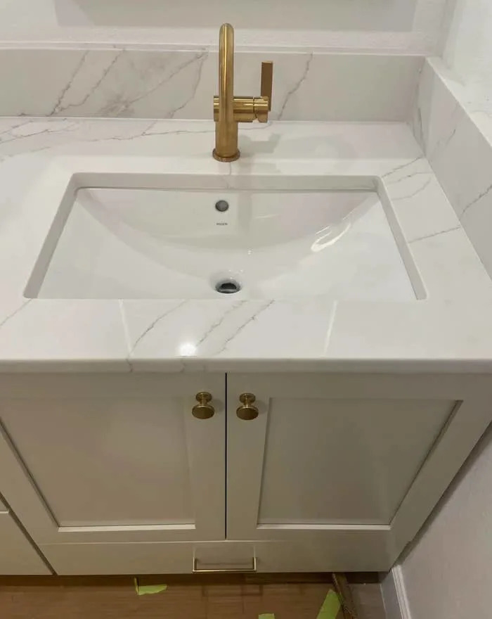 Bathroom vanity with a white marble worktop, a modern rectangular sink and an elegant gold tap