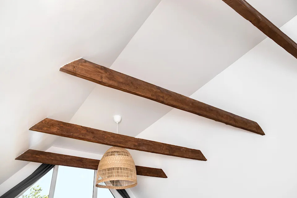 Ceiling view with wooden beams and a hanging rattan pendant, near a large window with curtains