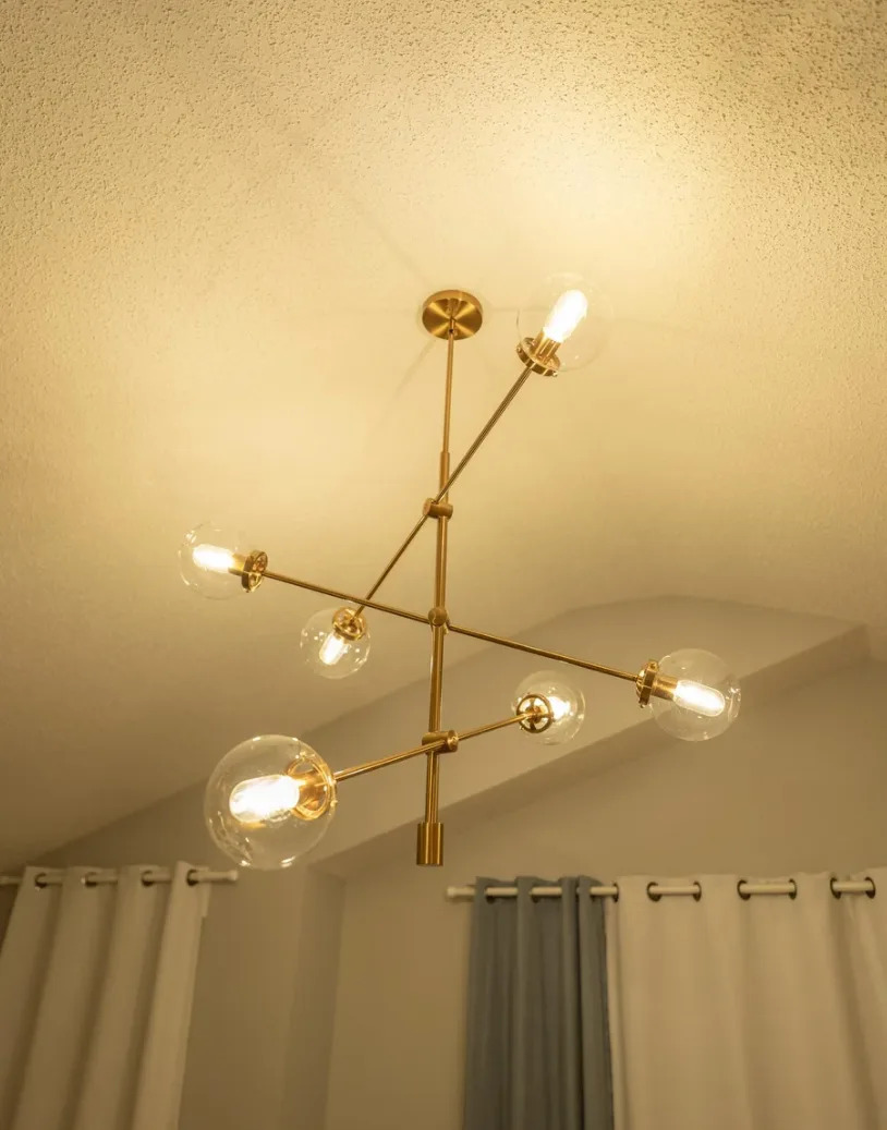 Modern chandelier with six exposed onions in a minimalist space with curtains and structured ceiling
