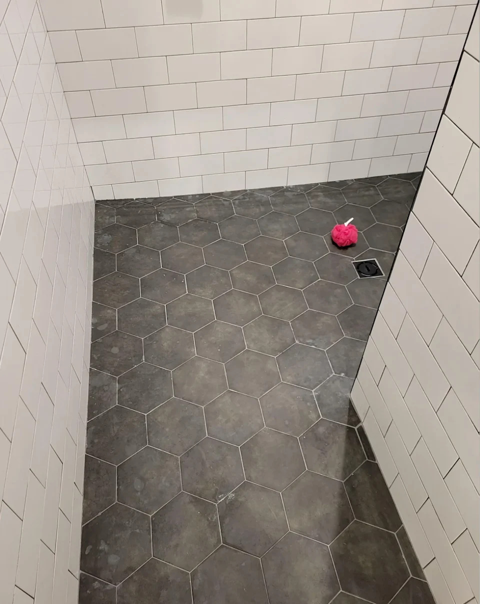 Bathroom with hexagonal floor tiles and white, tiled walls. A pink object is located on the floor near a drainage