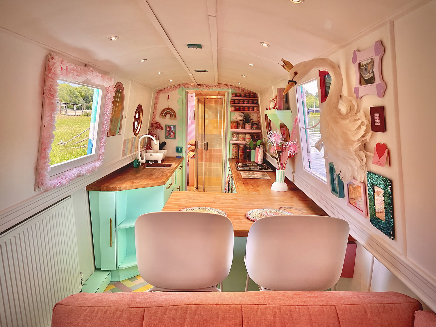 An interior view of a lively, colorful houseboat kitchen and a living area with light green cupboards, wooden panels and decorative elements such as a sway head and framed art.