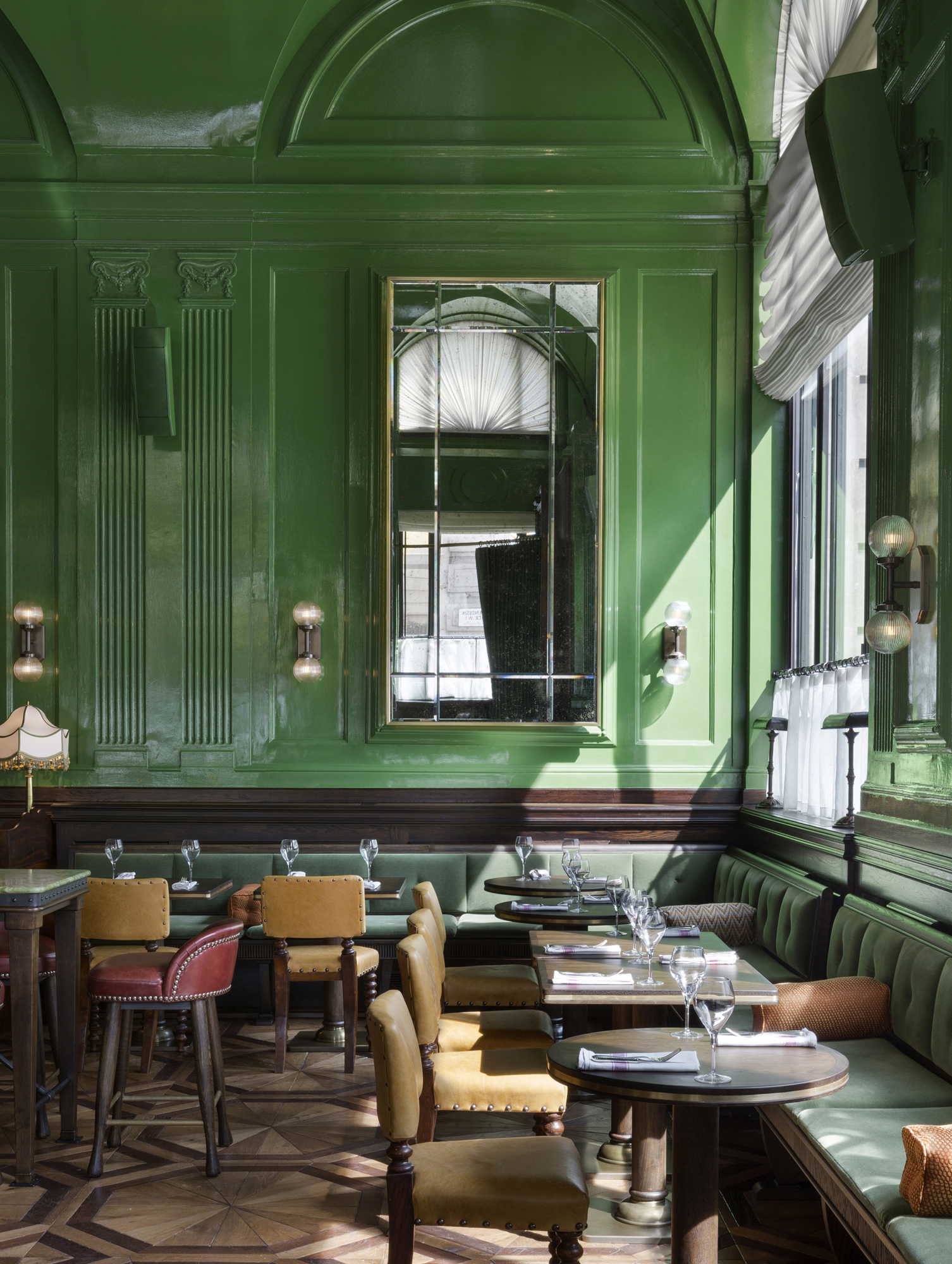 A restaurant interior with green walls, green, padded banquets and round wooden tables with leather chairs.