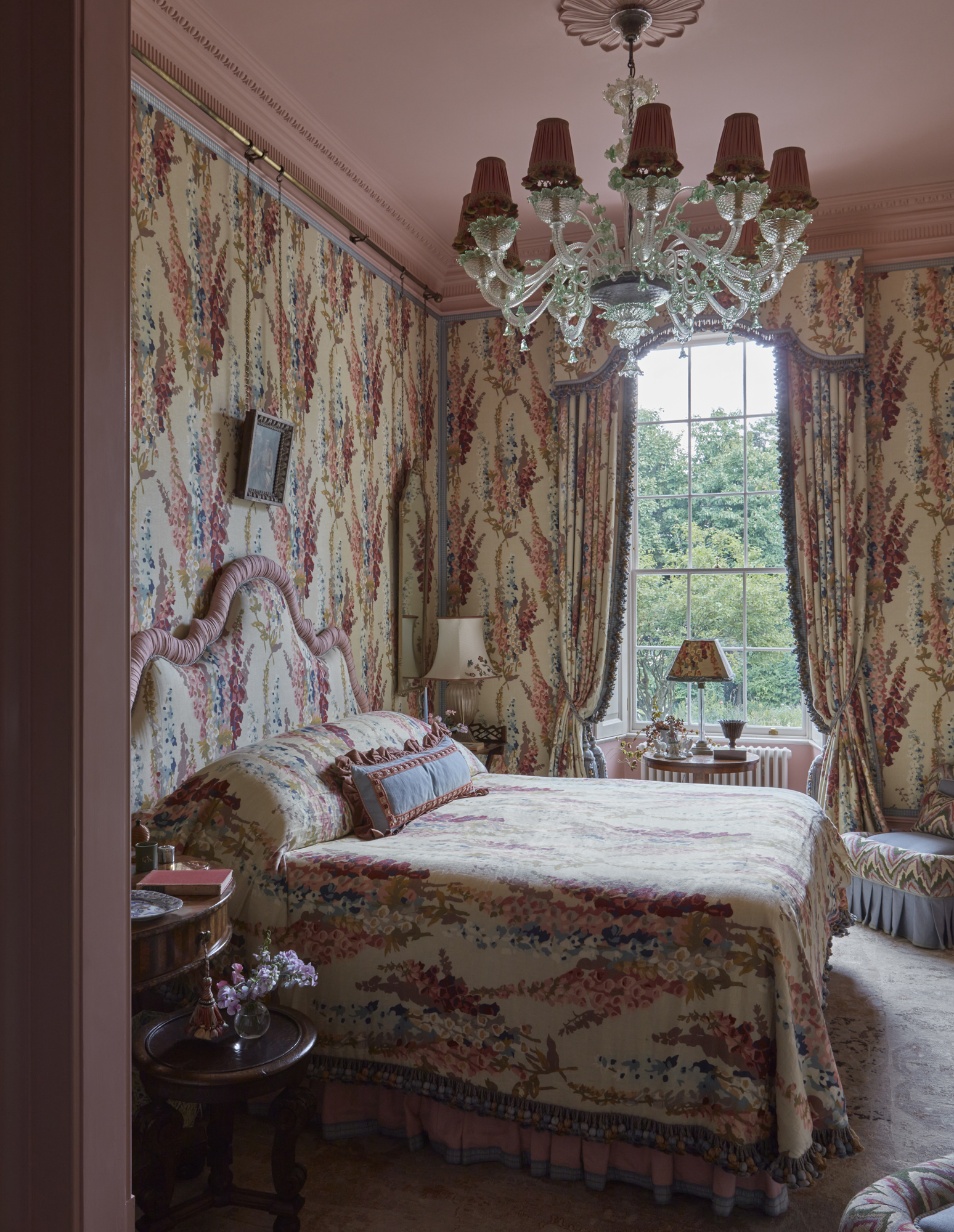 A bedroom with pink walls and ceiling with Jean Monro Lustmore Print on the walls, curtains and headboard.